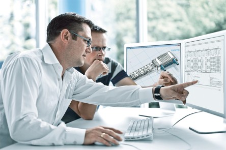 两位男士在办公室里查看电脑屏幕上的技术图纸和 3D 建模。