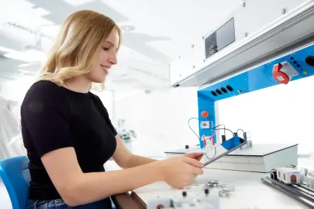 Learner checks data on a tablet while working on an electrical engineering setup.