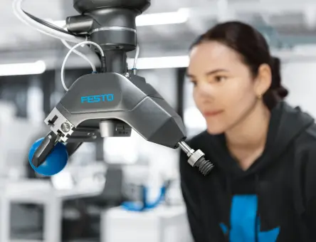 Festo adaptive gripper on a robot arm, shown in front of a female engineer during an automation test setup.