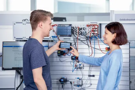 Learners review readings on a handheld device at an automation setup.