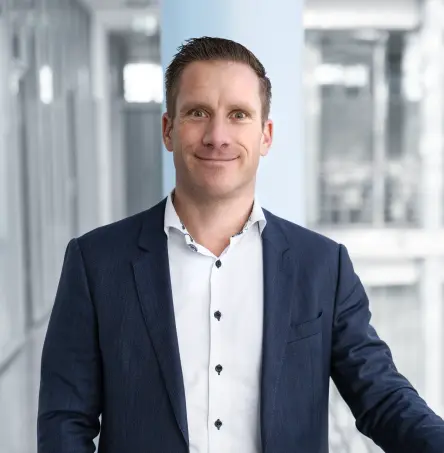 Christian Van Boxtel 站在现代风格的办公走廊里，面向镜头微笑。